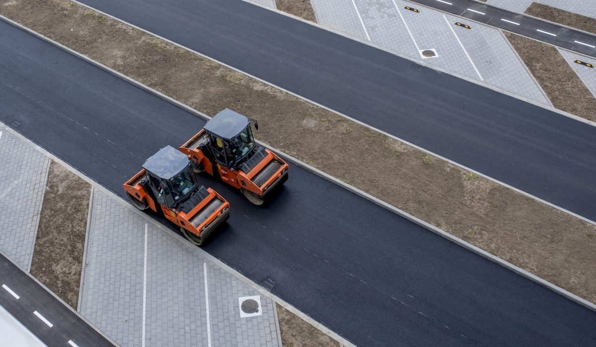 An aerial view of orange vibratory asphalt roller compactor on a new pavement